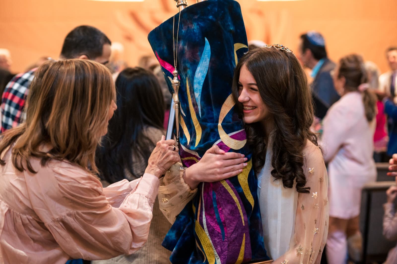 A bat mitzvah girl smiling as she embraces the Torah scroll in the sanctuary