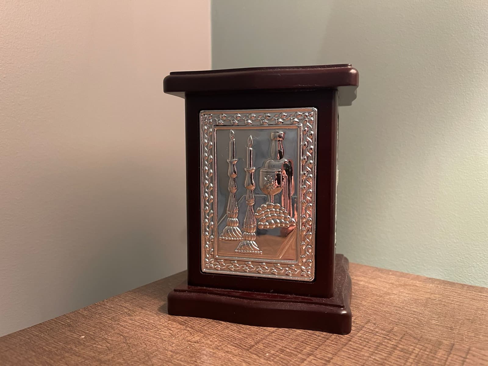 A wooden Tzedakah box with an embossed silver panel of Shabbat candlesticks and kiddush cup