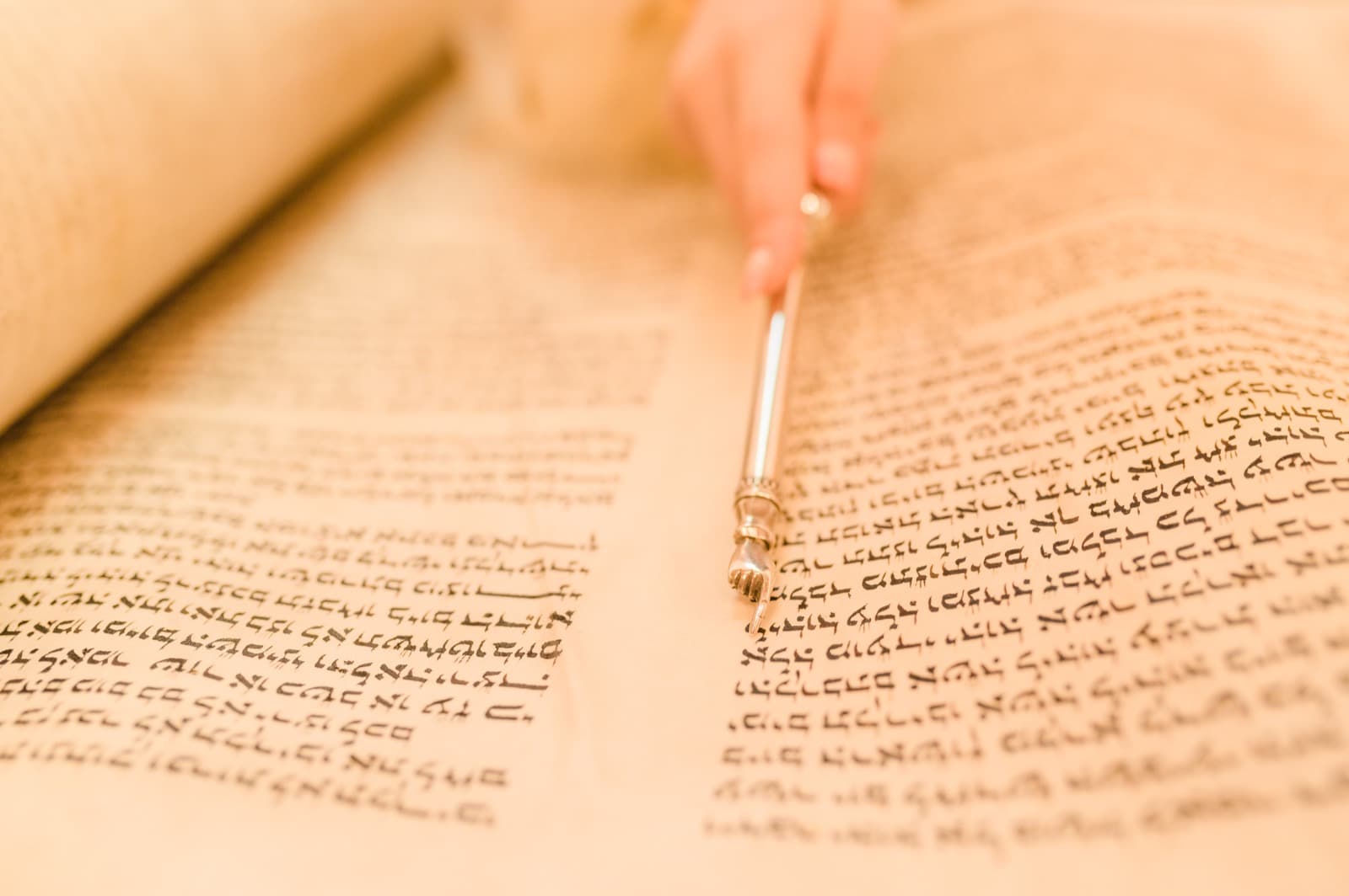 A silver yad tracing the handwritten Hebrew text of an open Torah scroll