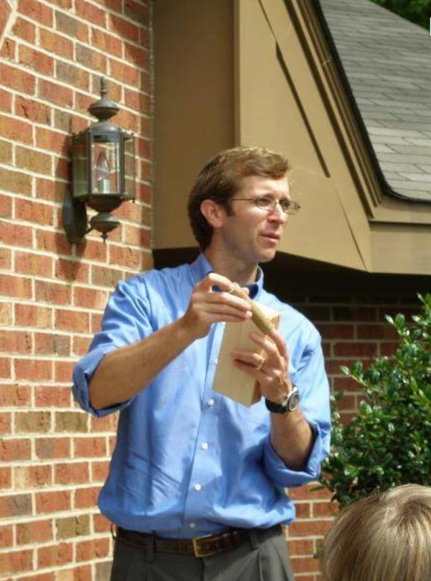 Rabbi Seth Klayman speaking at the entrance of the new building, holding the mezuzah before its installation