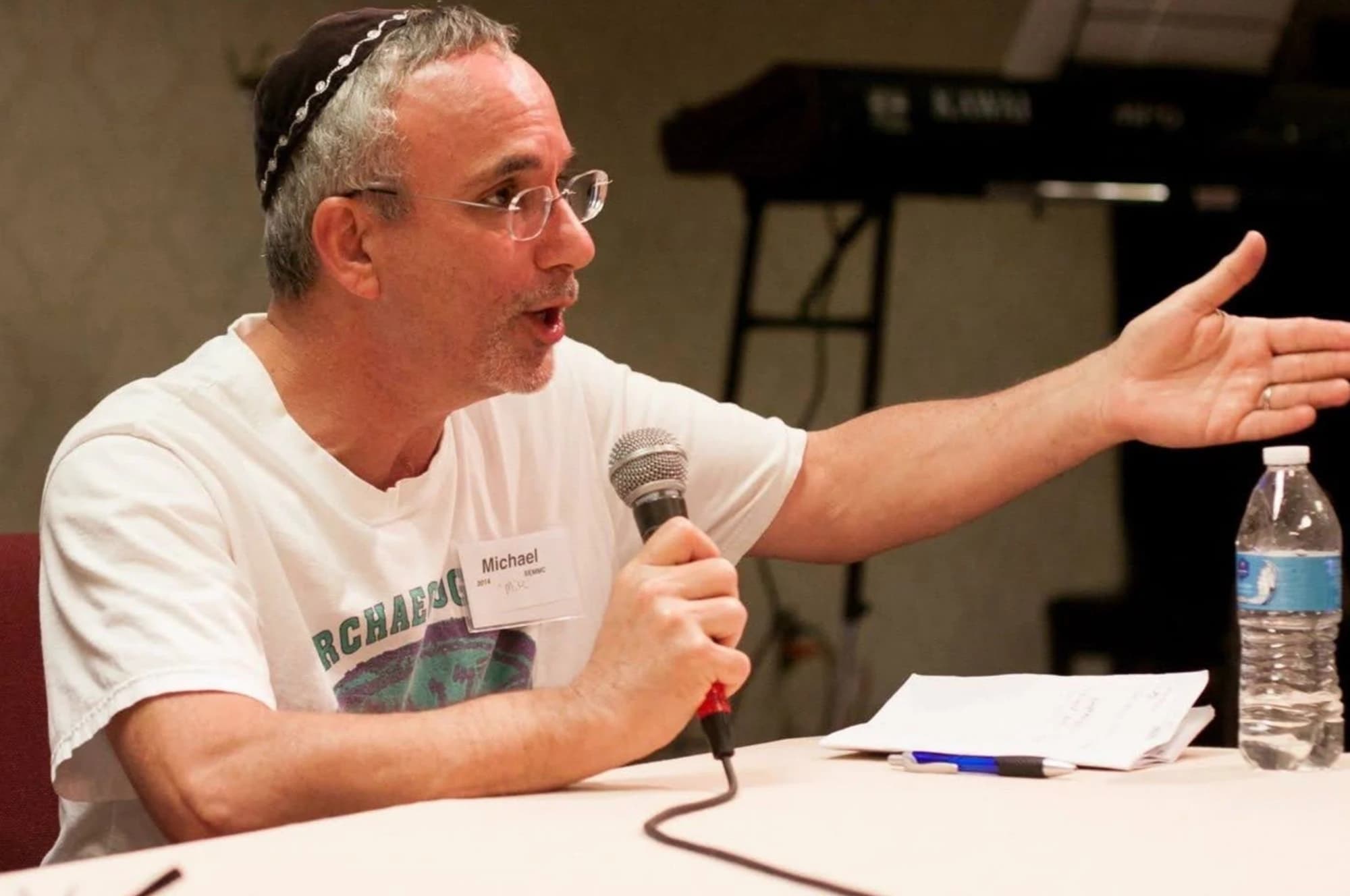 Reb Mike Kaufman in the congregation's early years, kippah on and microphone in hand, teaching from a panel table