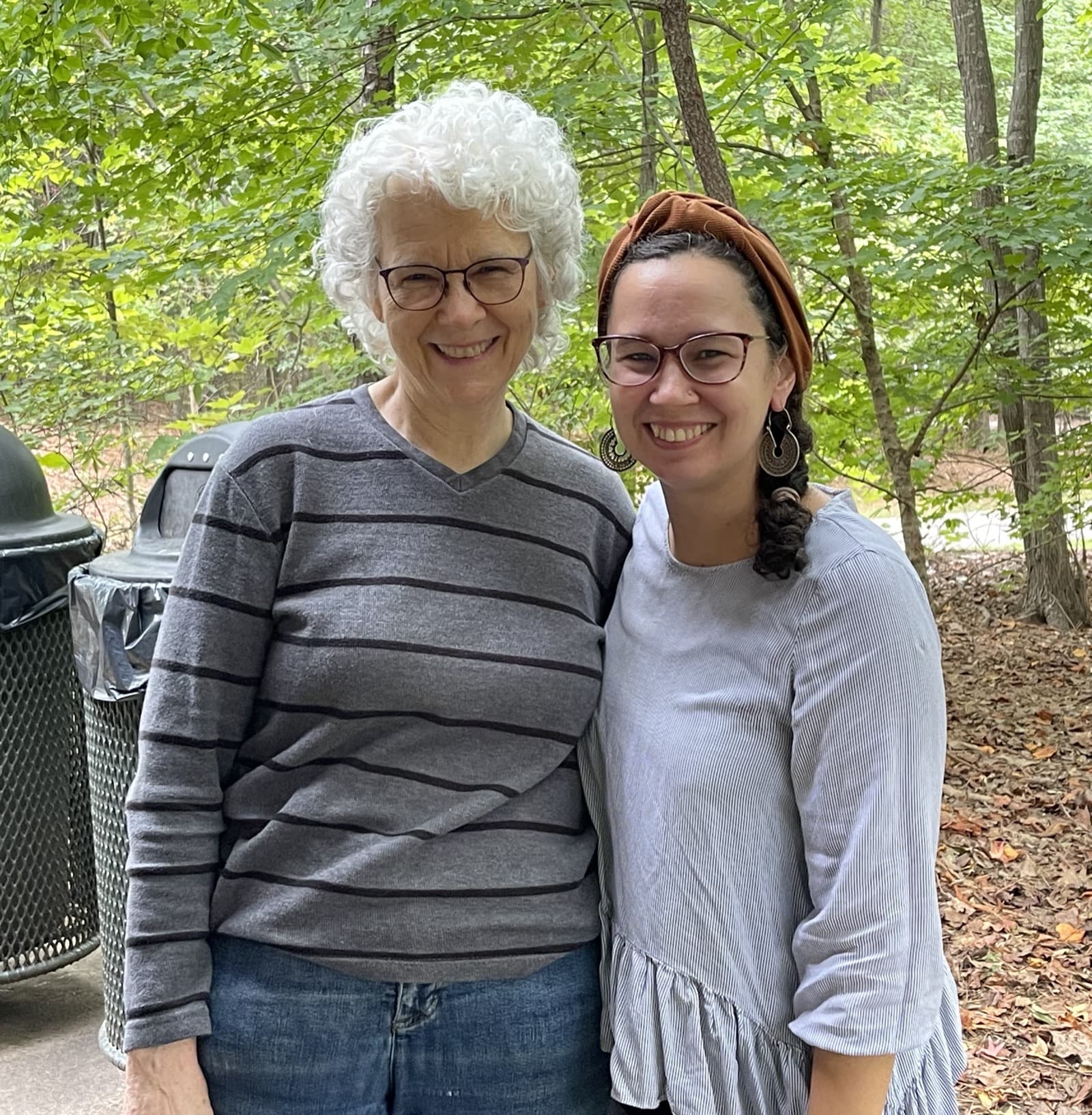Two members of the congregation, arm in arm, smiling together outdoors among the trees