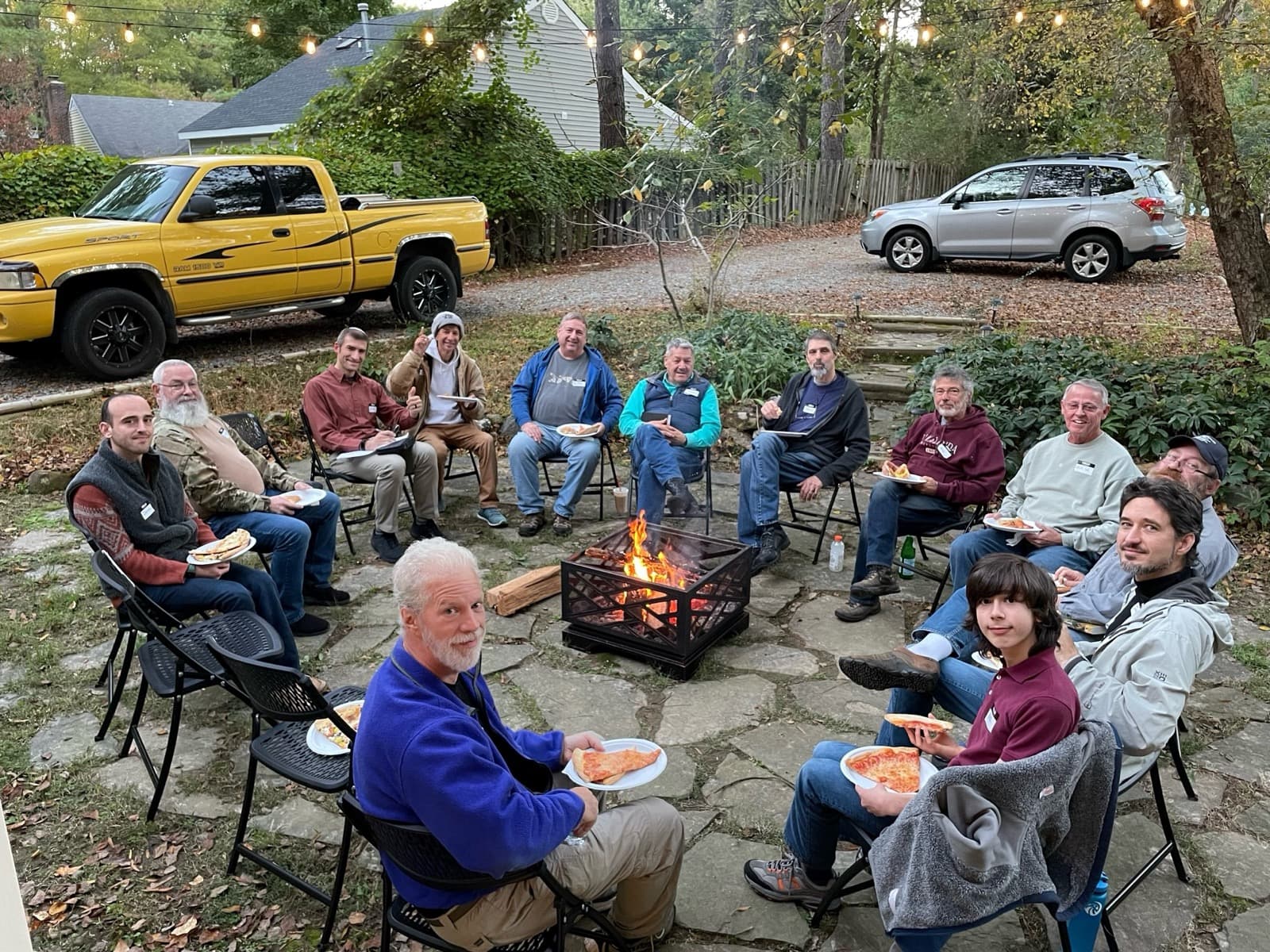 Men of Sha'arei Shalom sharing pizza around a fire pit at an evening fellowship gathering