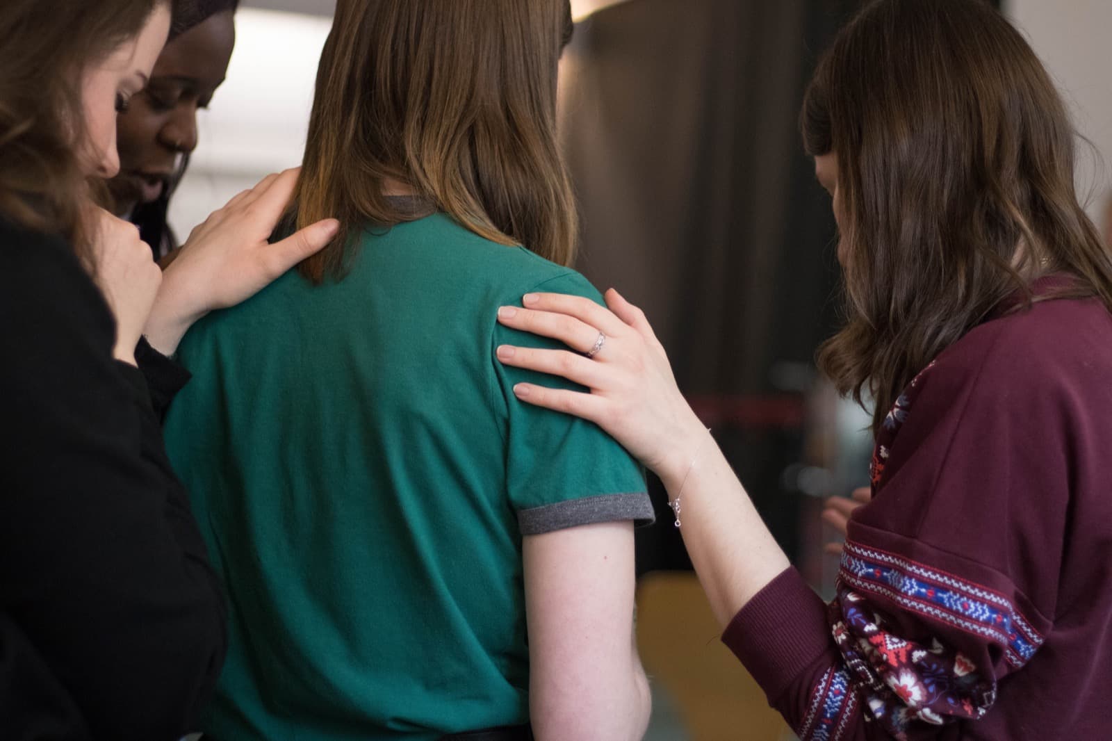 Women gathered close in prayer, hands resting on a friend's shoulders
