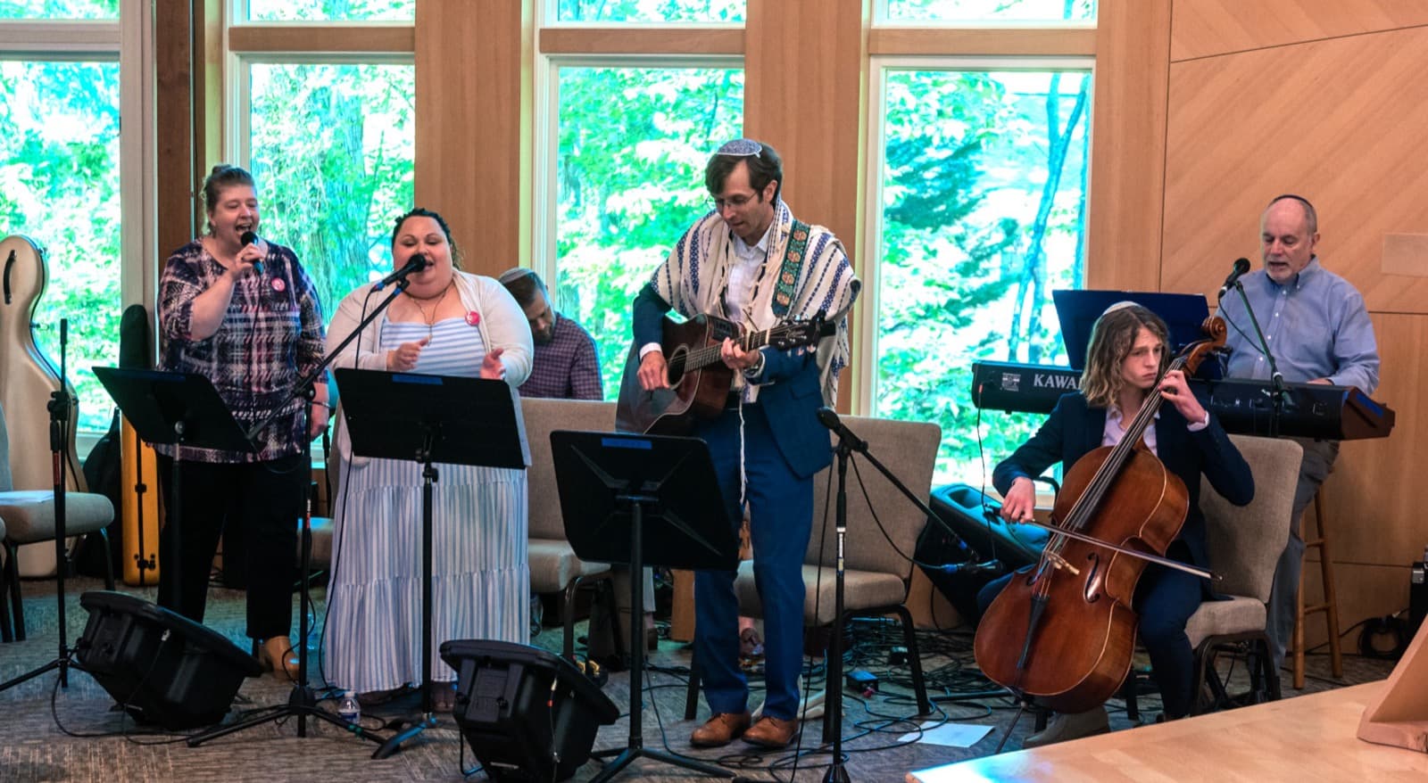 The worship ensemble—vocalists, guitar, cello, and keyboard—leading music before the sanctuary windows on Shabbat