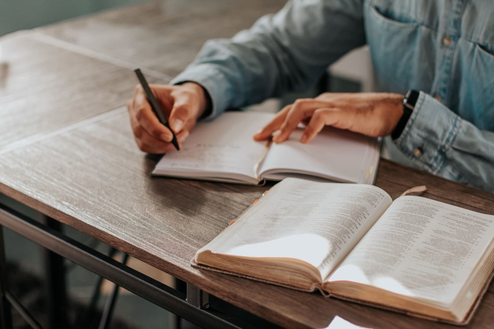 Taking handwritten notes beside an open Bible at a study table